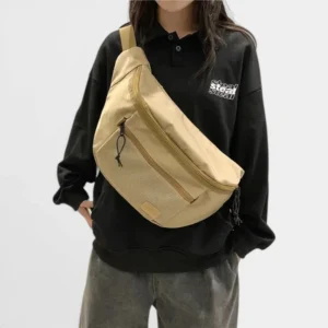 Grand sac banane XXL en nylon beige porté en bandoulière par une femme au style streetwear décontracté, de face