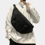 Grand Sac Banane XXL Streetwear Sac banane XXL noir en nylon porté en bandoulière par un homme au style streetwear urbain-décontracté, vu de face