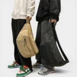 Grand Sac Banane XXL Streetwear Grand sac banane XXL en nylon beige et noir tenu à la main par deux personnes au style streetwear