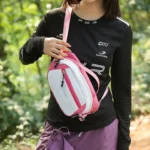 Sac Banane Bicolore Randonnée Nylon Léger Femme saisissant par la poignée un sac banane bicolore blanc et rose porté en bandoulière.