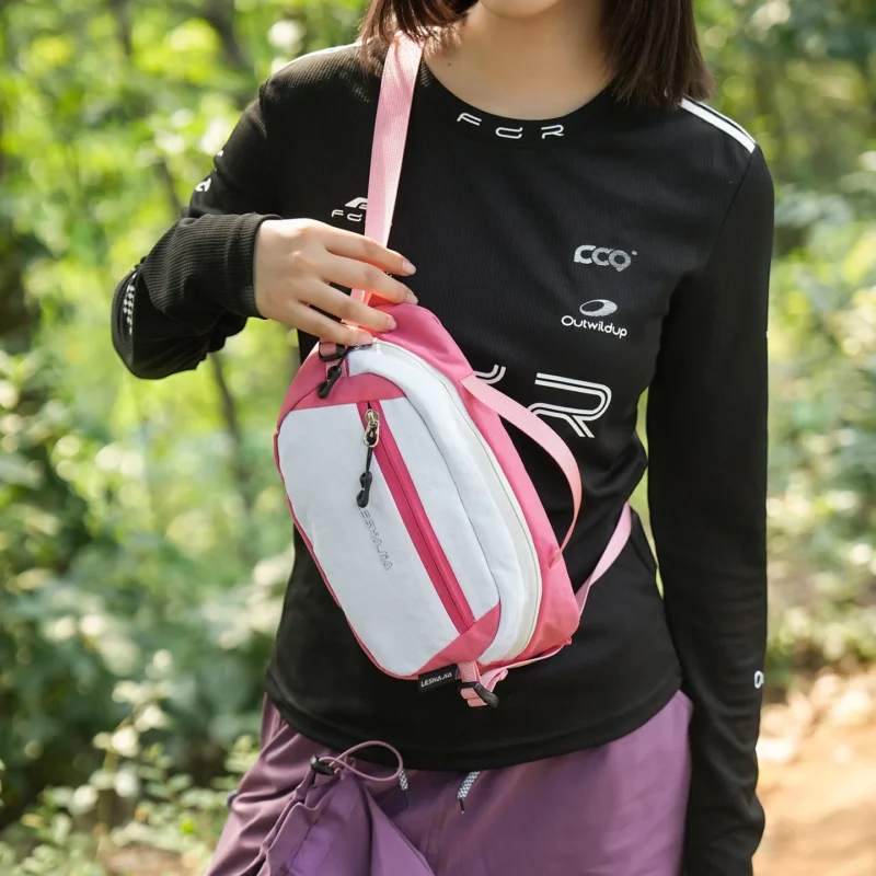 Femme saisissant par la poignée un sac banane bicolore blanc et rose porté en bandoulière.