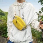 Sac Banane Bicolore Randonnée Nylon Léger Homme portant un sac banane bicolore jaune et crème en bandoulière sur la poitrine, en randonnée.