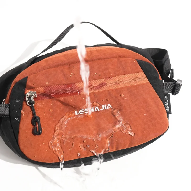 Eau versée sur un sac banane bicolore orange et noir, les gouttes perlent à la surface du tissu.