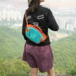 Sac Banane Bicolore Randonnée Nylon Léger Femme de dos portant un sac banane bicolore turquoise et orange basculé dans le dos.
