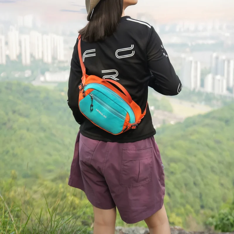 Femme de dos portant un sac banane bicolore turquoise et orange basculé dans le dos.