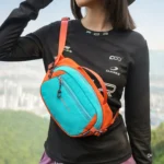 Sac Banane Bicolore Randonnée Nylon Léger Femme portant un sac banane bicolore turquoise et orange en bandoulière sur la poitrine.