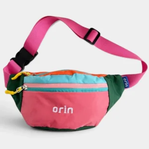 Sac banane enfant en nylon rose à panneaux verts et bleus, suspendu par sa sangle et vu de trois-quarts.
