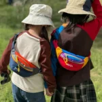 Sac banane enfant en nylon rouge et bleu porté en bandoulière dans le dos par deux enfants en balade.