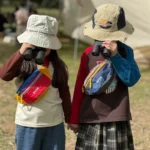 Sac banane enfant en nylon rouge et bleu porté en bandoulière par deux enfants aux jumelles.
