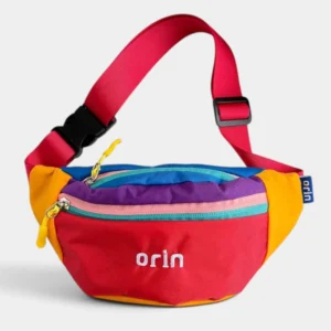 Sac banane enfant en nylon rouge à empiècements colorblock, suspendu par sa sangle et vu de trois-quarts.