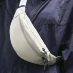 Sac Banane Nylon Satiné Léger Sac banane nylon satiné gris clair porté en bandoulière vu en gros plan sur la poitrine