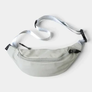 Sac banane nylon satiné gris clair posé à plat vu de dessus avec sangle blanc cassé et boucle noire