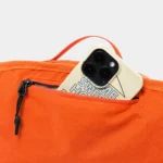 Sac banane orange en gros plan sur la poche arrière ouverte avec un téléphone glissé dedans