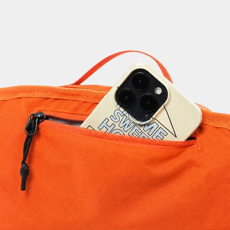 Sac banane orange en gros plan sur la poche arrière ouverte avec un téléphone glissé dedans