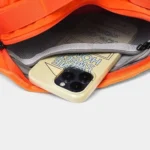 Sac banane orange ouvert sur sa poche filet zippée intérieure avec un téléphone glissé dedans