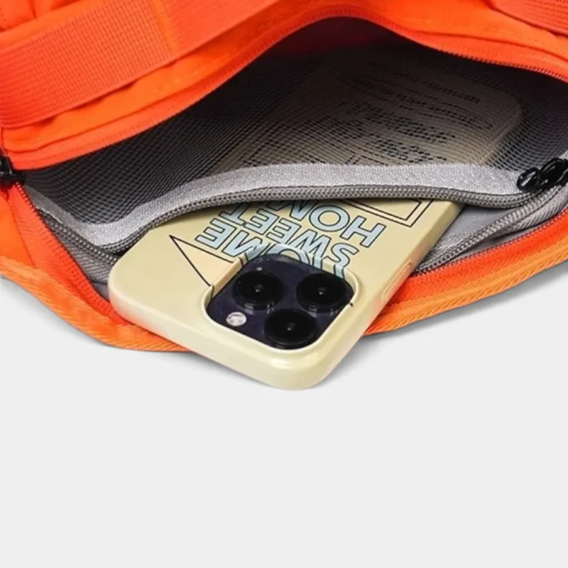 Sac banane orange ouvert sur sa poche filet zippée intérieure avec un téléphone glissé dedans