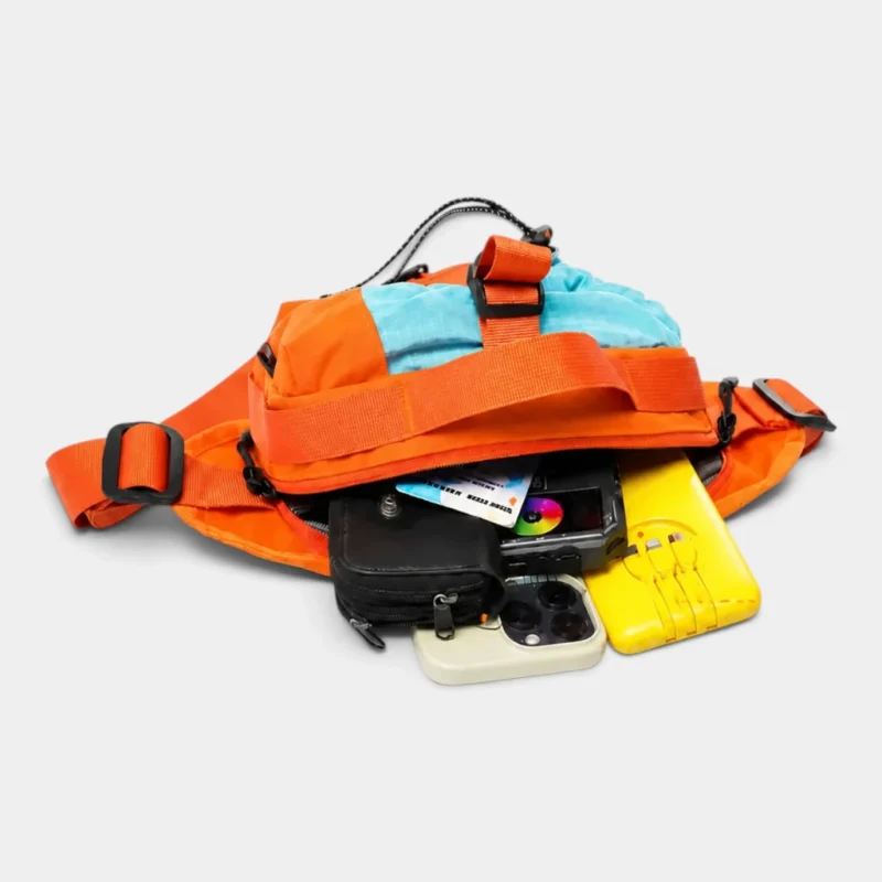 Sac banane orange vu de dessus avec sa poche principale ouverte sur un téléphone et un portefeuille