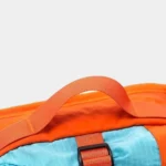 Sac banane orange en gros plan sur la poignée de portage sanglée et le panneau ripstop bleu ciel
