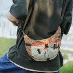Sac Banane Randonnée Ultraléger Double Sangle Sac banane beige et vert porté en bandoulière par un homme de profil sur un point de vue urbain