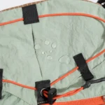 Sac Banane Randonnée Ultraléger Double Sangle Sac banane en nylon vert amande vu de très près avec gouttes d'eau perlant sur le tissu et cordon élastique orange