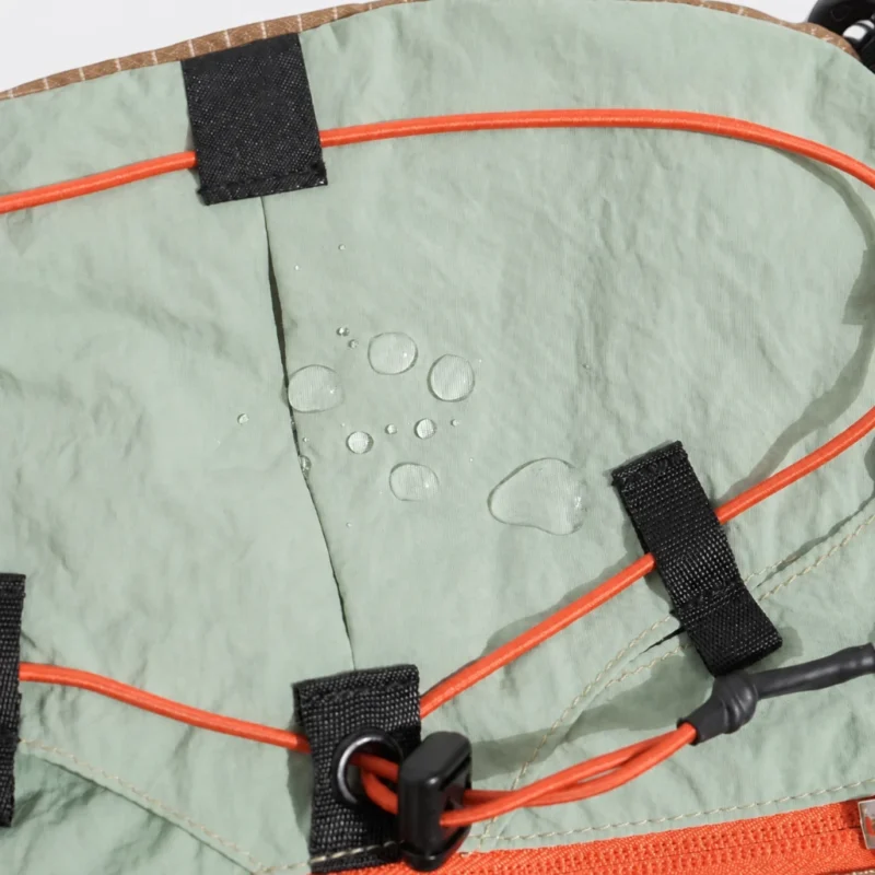Sac banane en nylon vert amande vu de très près avec gouttes d'eau perlant sur le tissu et cordon élastique orange