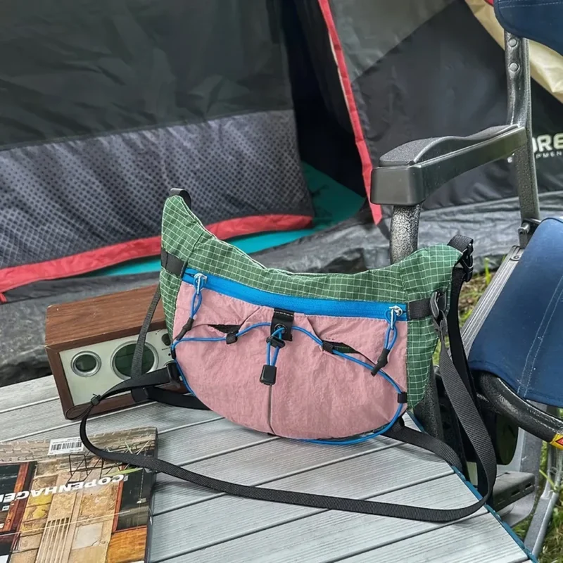 Sac banane vert et rose en nylon ripstop posé sur une table de camping devant une tente
