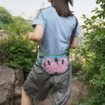 Sac Banane Randonnée Ultraléger Double Sangle Sac banane vert et rose porté dans le dos par une femme en randonnée sur un sentier rocheux