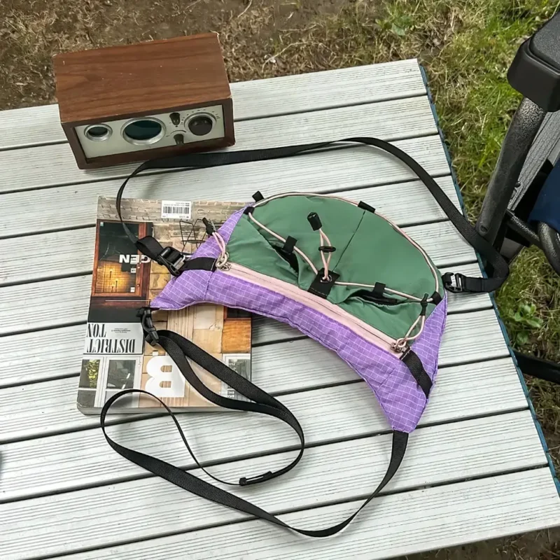 Sac banane violet et vert posé à plat vu de dessus avec sa sangle principale déployée