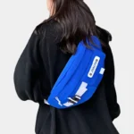 Grand Sac Banane Techwear Bleu Roi Sac banane techwear en nylon porté en bandoulière dans le dos par une femme avec sangle de façade blanche
