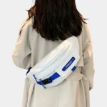 Sac banane techwear en nylon blanc porté en bandoulière dans le dos par une femme avec boucle clip noire