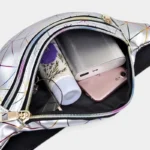 Sac Banane Géométrique Multicolore Brillant Festival Sac banane en cuir argenté ouvert vu de dessus, révélant une batterie externe et un smartphone