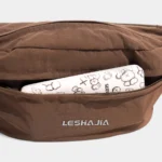 Sac Banane Coupe-Vent Années 90 Déperlant Gros plan sur la poche avant zippée du sac banane coupe-vent années 90 marron, avec un téléphone rangé dedans