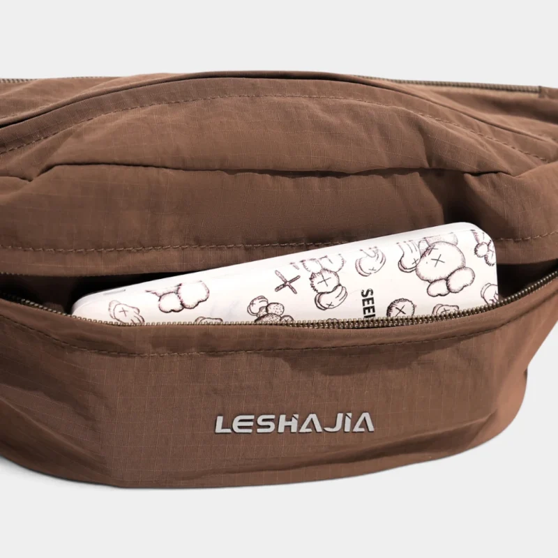 Gros plan sur la poche avant zippée du sac banane coupe-vent années 90 marron, avec un téléphone rangé dedans