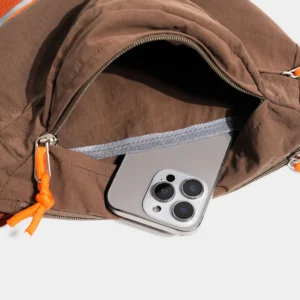 Sac banane coupe-vent années 90 marron vu de près, poche zippée ouverte sur un smartphone glissé à l'intérieur