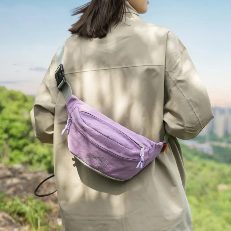 Sac banane coupe-vent années 90 violet lilas porté en bandoulière dans le dos par une femme sur un sentier