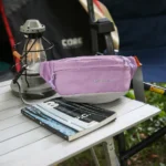 Sac Banane Coupe-Vent Années 90 Déperlant Sac banane coupe-vent années 90 violet lilas posé de trois quarts sur une table de camping, poche avant zippée