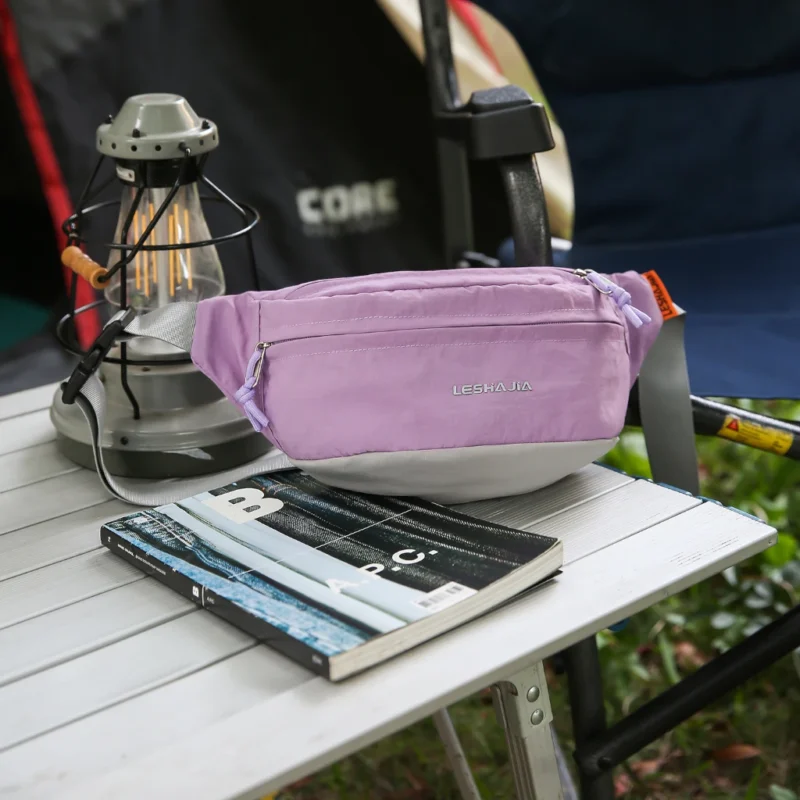 Sac banane coupe-vent années 90 violet lilas posé de trois quarts sur une table de camping, poche avant zippée