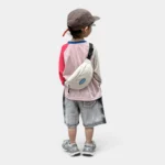 Sac banane enfant en toile de nylon blanc cassé porté en bandoulière dans le dos par un petit garçon vu de dos