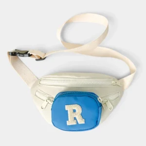 Sac banane enfant crème posé à plat de face avec poche avant bleue et lettre R en bouclette