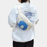 Sac Banane Enfant Multipoche Lettre Brodée Sac banane enfant crème à poche avant bleue porté en bandoulière dans le dos par un enfant