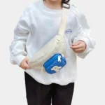 Sac Banane Enfant Multipoche Lettre Brodée Sac banane enfant crème à poche avant bleue porté en bandoulière sur la poitrine par un enfant