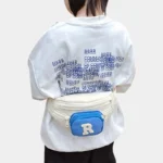Sac Banane Enfant Multipoche Lettre Brodée Sac banane enfant crème à poche avant bleue porté à la taille dans le dos par un enfant