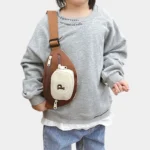 Sac Banane Enfant Multipoche Lettre Brodée Sac banane enfant marron à poche avant crème porté en bandoulière verticale sur la poitrine d'un enfant