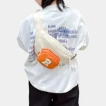 Sac Banane Enfant Multipoche Lettre Brodée Sac banane enfant crème à poche avant orange porté en bandoulière dans le dos par un enfant