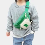 Sac Banane Enfant Multipoche Lettre Brodée Sac banane enfant vert à poche avant crème porté en bandoulière sur la poitrine par un enfant