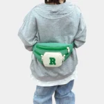 Sac Banane Enfant Multipoche Lettre Brodée Sac banane enfant vert à poche avant crème porté à la taille dans le dos par un enfant