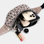 Sac banane doré métallique en PVC, poche principale ouverte révélant un smartphone et des cosmétiques, posé à plat