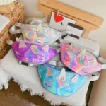 Sacs banane licorne holographiques blanc nacré, violet, rose et turquoise posés ensemble sur un plaid gaufré