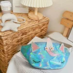 Sac banane licorne holographique turquoise posé sur un livre près de coussins lune et étoile
