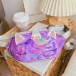 Sac banane licorne holographique violet posé sur un panier en osier près d'une lampe de chevet